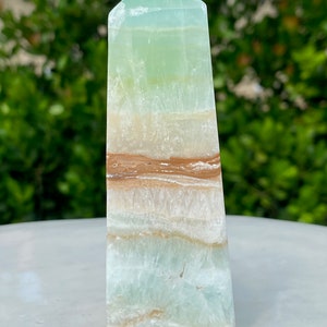 May include: A green, white, and brown banded obelisk crystal point. The crystal is polished and has a smooth, glassy surface.