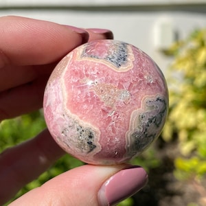 May include: Pink and gray sphere of polished pink manganese, a type of gemstone, with a swirling pattern.