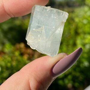 May include: A clear, light blue aquamarine crystal with a rectangular shape. The crystal has a smooth, polished surface and is translucent.