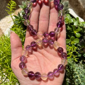 Puede incluir: Dos pulseras hechas con cuentas de piedras preciosas moradas y amarillas. Las pulseras est&aacute;n apiladas una encima de la otra en la mu&ntilde;eca de una persona.
