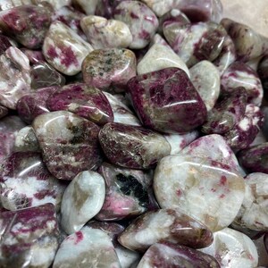 May include: A collection of tumbled pink and white stones with a variety of patterns and textures. The stones are smooth and polished, and they have a natural, earthy look.