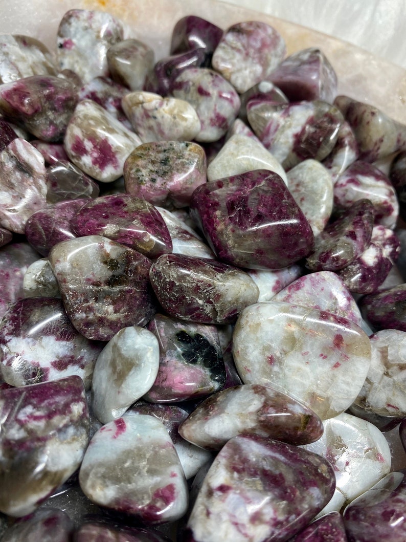 May include: A collection of tumbled pink and white stones with a variety of patterns and textures. The stones are smooth and polished, and they have a natural, earthy look.