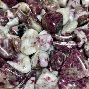 May include: A collection of tumbled pink and white stones with a speckled pattern. The stones are smooth and polished, and they have a natural, organic look.