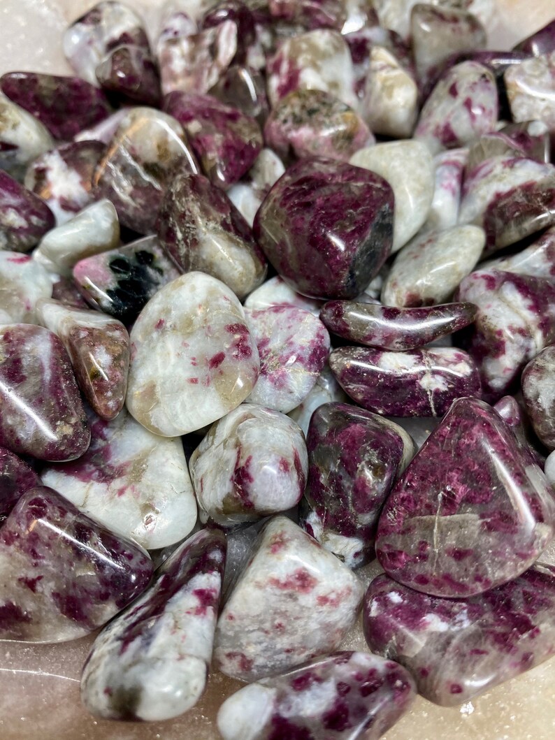 May include: A collection of tumbled pink and white stones with a speckled pattern. The stones are smooth and polished, and they have a natural, organic look.
