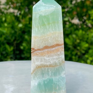 May include: A green and white banded obelisk crystal point with brown and orange banding. The crystal is polished and has a smooth, glassy surface.