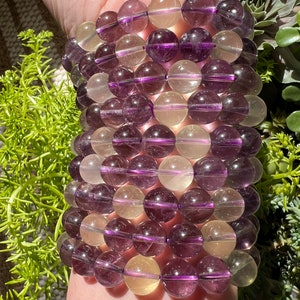 Puede incluir: Un brazalete hecho de cuentas redondas de piedras preciosas de color p&uacute;rpura y amarillo. Las cuentas son transl&uacute;cidas y tienen un ligero brillo.