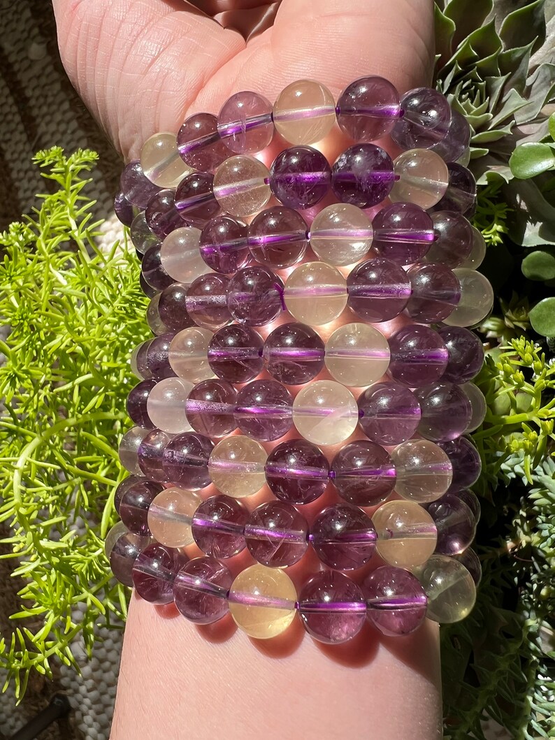 Puede incluir: Un brazalete hecho de cuentas redondas de piedras preciosas de color p&uacute;rpura y amarillo. Las cuentas son transl&uacute;cidas y tienen un ligero brillo.