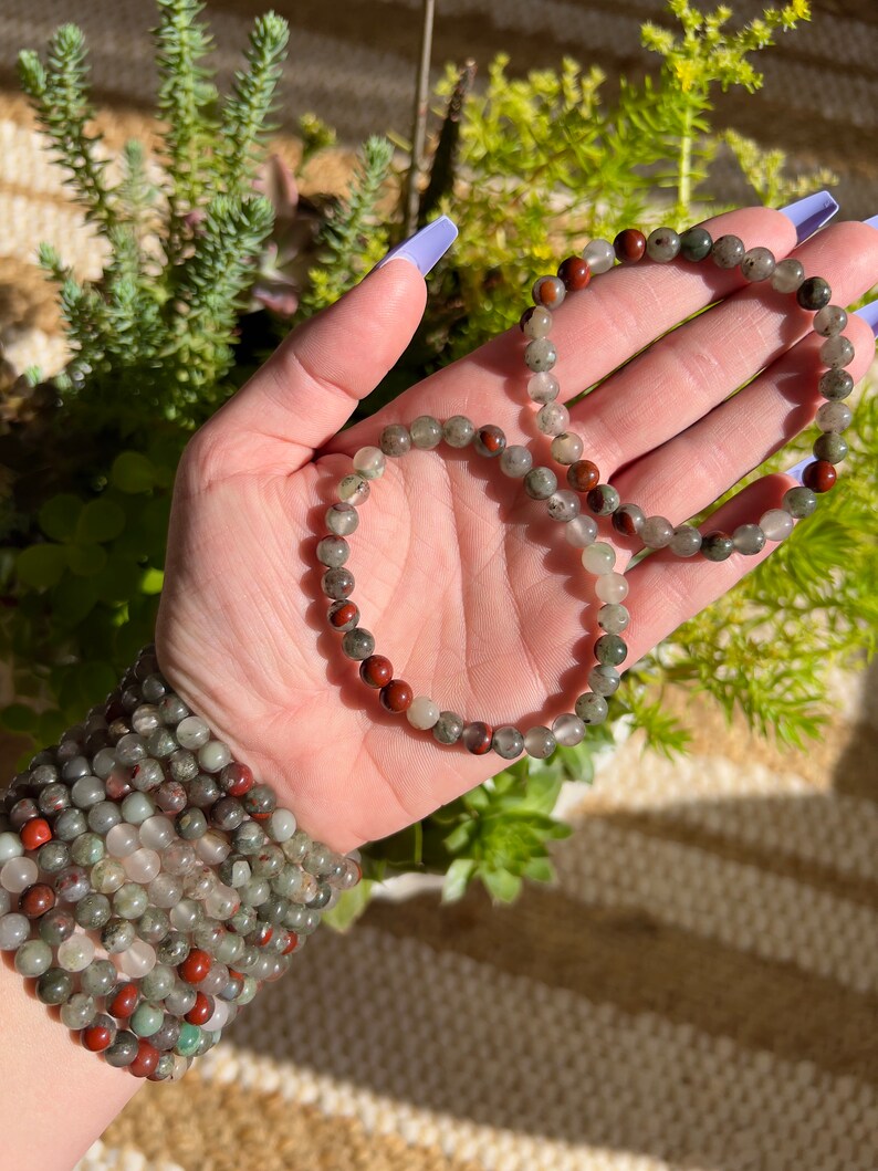 Pu&ograve; includere: Due braccialetti fatti di perline verdi, rosse e trasparenti. I braccialetti sono impilati uno sopra l'altro e sono tenuti da una mano.