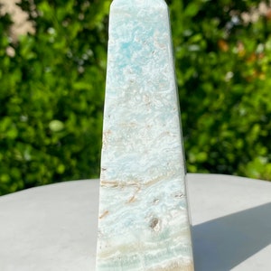 May include: A light blue celestite obelisk with white and brown swirls. The obelisk is polished and has a pointed top.