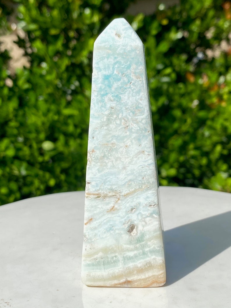 May include: A light blue celestite obelisk with white and brown swirls. The obelisk is polished and has a pointed top.
