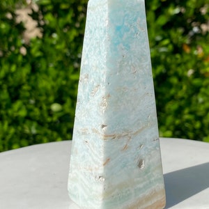 May include: A light blue and white celestite crystal pyramid, also known as an obelisk, with a smooth, polished finish.