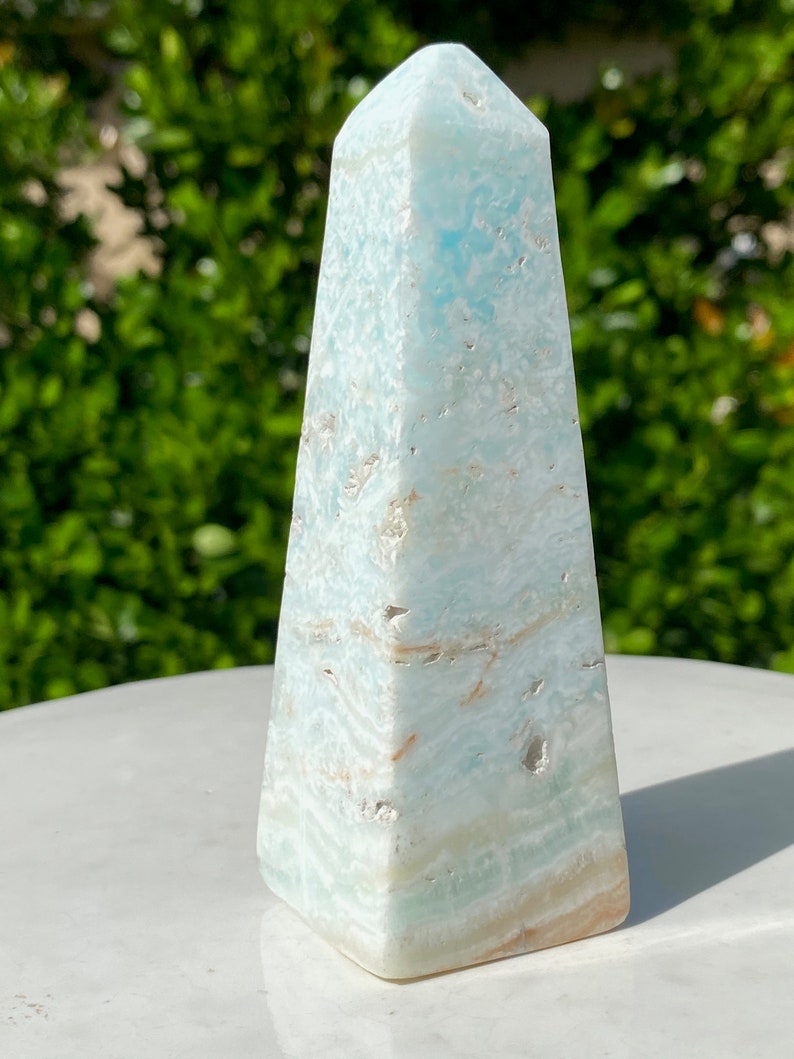 May include: A light blue and white celestite crystal pyramid, also known as an obelisk, with a smooth, polished finish.
