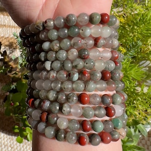 Pu&ograve; includere: Un set di braccialetti realizzati con perline di pietre preziose verdi, rosse e bianche. I braccialetti sono indossati al polso.