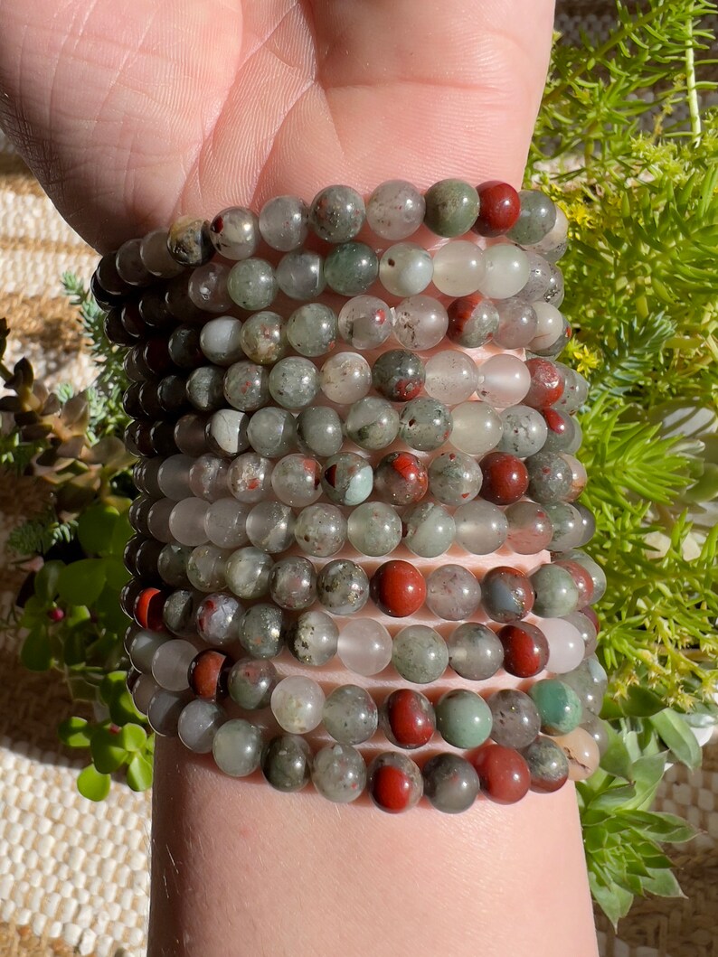 Pu&ograve; includere: Un set di braccialetti realizzati con perline di pietre preziose verdi, rosse e bianche. I braccialetti sono indossati al polso.