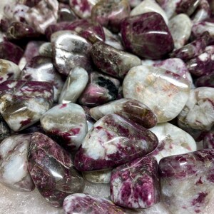 May include: A collection of tumbled pink and white stones with a variety of patterns and textures. The stones are smooth and polished, and they have a natural, earthy look.