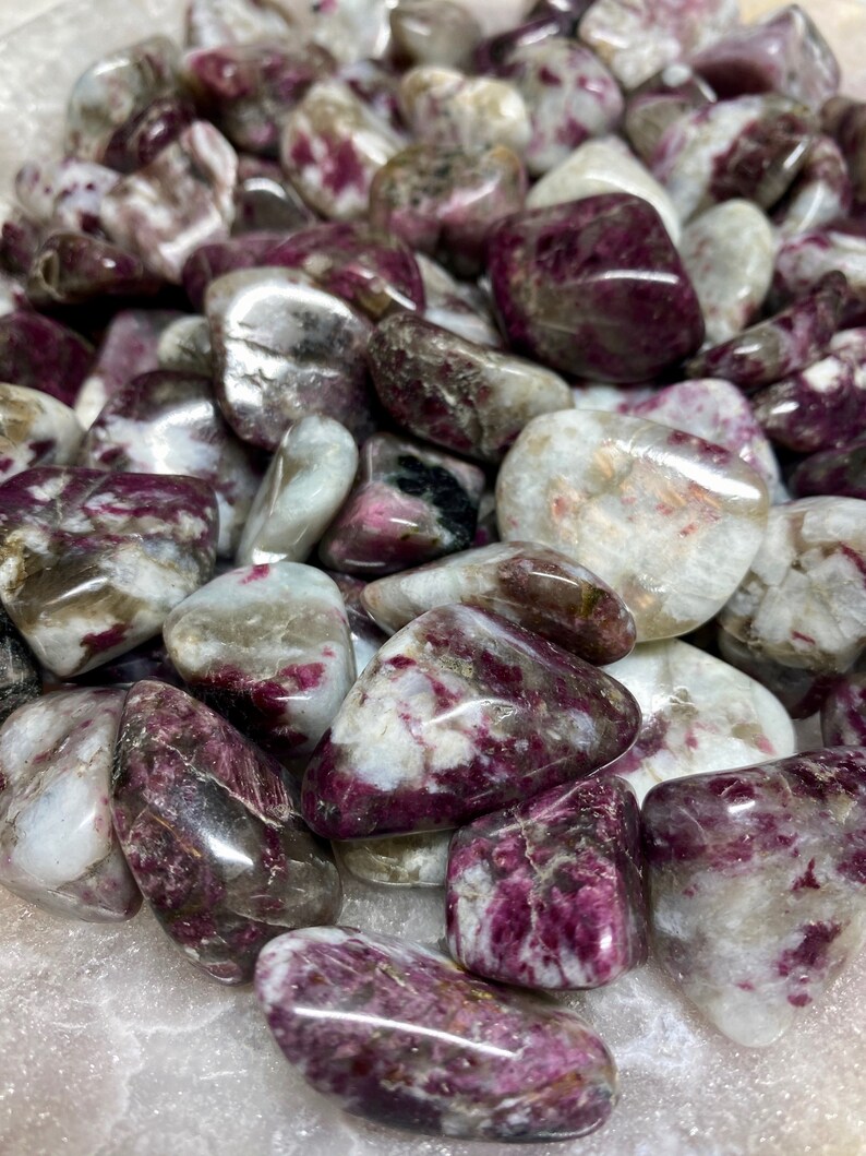 May include: A collection of tumbled pink and white stones with a variety of patterns and textures. The stones are smooth and polished, and they have a natural, earthy look.