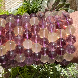 Puede incluir: Un brazalete hecho de cuentas redondas, transl&uacute;cidas, de color morado y blanco. Las cuentas est&aacute;n apiladas en filas, creando un efecto de capas. El brazalete se lleva en la mu&ntilde;eca.