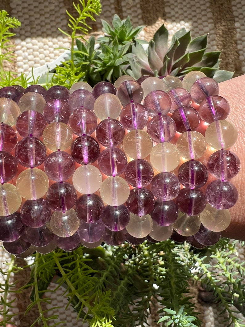 Puede incluir: Un brazalete hecho de cuentas redondas, transl&uacute;cidas, de color morado y blanco. Las cuentas est&aacute;n apiladas en filas, creando un efecto de capas. El brazalete se lleva en la mu&ntilde;eca.
