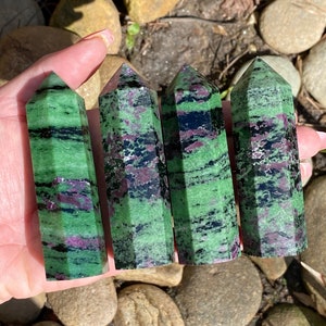 Peut inclure: Quatre pointes de cristal de zoïsite vertes, noires et roses. Les pointes sont lisses et polies, avec une variété de stries et de motifs.