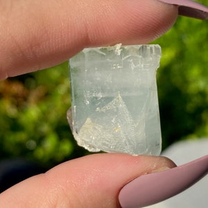 May include: A clear, light blue aquamarine crystal with a slightly cloudy appearance. The crystal is faceted and has a rectangular shape.
