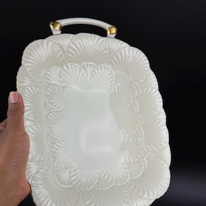 May include: A white ceramic serving tray with a scalloped edge design. The tray has two handles with gold accents. The tray is rectangular with a smooth, glossy surface and a decorative, textured border.