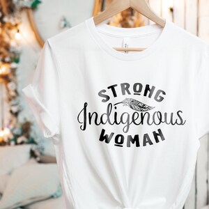 May include: White t-shirt with black text that reads "STRONG Indigenous WOMAN" and a stylized feather graphic.