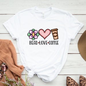 May include: White t-shirt with a flower, heart, and coffee cup graphic. The text "Bead Love Coffee" is printed below the graphic.