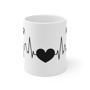May include: White ceramic mug with a black heartbeat graphic and a black heart in the center. The heartbeat graphic is a stylized representation of an electrocardiogram.