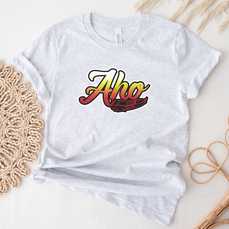 May include: A gray t-shirt with the word "Aho" in a stylized font with a red, orange, and yellow gradient. A black and white feather design is below the word.