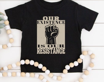 May include: Black t-shirt with a beige graphic of a raised fist and the text "OUR EXISTENCE IS OUR RESISTANCE".