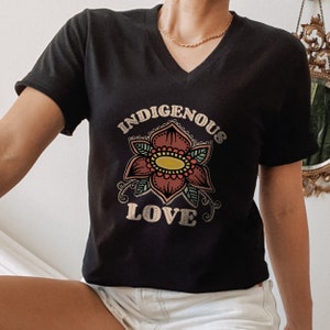 May include: Black v-neck t-shirt with a stylized flower graphic and the text "Indigenous Love" in a vintage font.