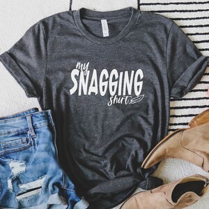 May include: A dark gray t-shirt with the text "my snagging shirt" in white lettering with a small feather design.