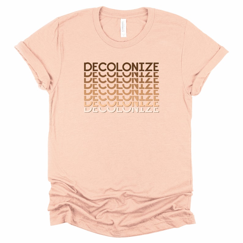 Puede incluir: Una camiseta rosa claro con la palabra "DECOLONIZE" repetida en un degradado de tonos marrones.
