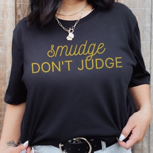 Puede incluir: Camiseta negra con el texto "smudge don't judge" en amarillo.