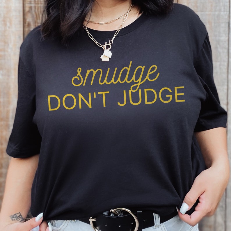 Puede incluir: Camiseta negra con el texto "smudge don't judge" en amarillo.