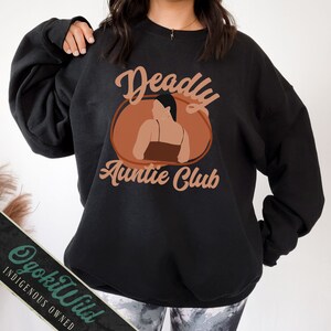 May include: Black sweatshirt with a brown circle graphic that says "Deadly Auntie Club" in a retro font. The graphic features a brown silhouette of a woman with long black hair.