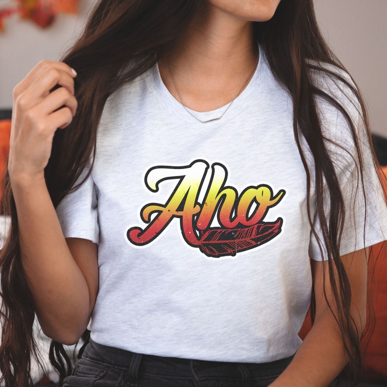 May include: A white t-shirt with a red, yellow, and orange graphic of the word "Aho" with a feather underneath.