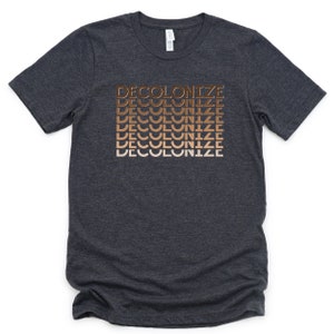 Puede incluir: Una camiseta gris oscuro jaspeada con la palabra "DECOLONIZE" repetida cinco veces en un degradado de tonos marrones.
