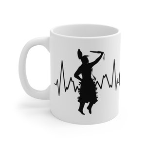 May include: White ceramic mug with a black silhouette of a Native American dancer holding a stick, with a heartbeat line behind the dancer.