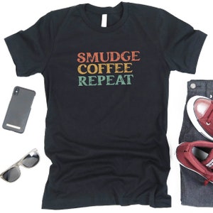 May include: Black t-shirt with the text "SMUDGE COFFEE REPEAT" in a retro font with orange, yellow, green, and blue colors.