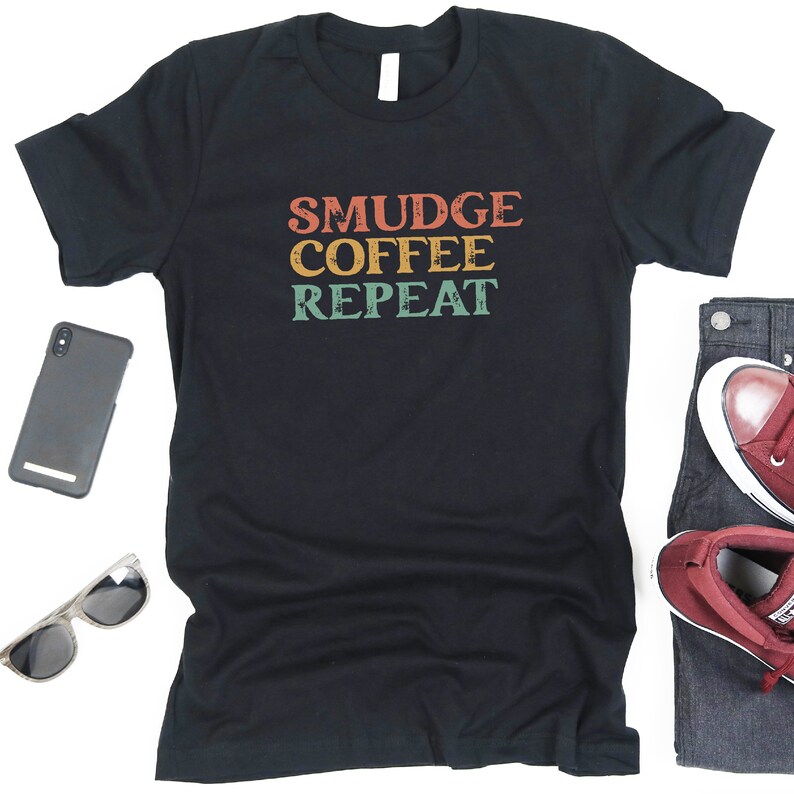 May include: Black t-shirt with the text "SMUDGE COFFEE REPEAT" in a retro font with orange, yellow, green, and blue colors.