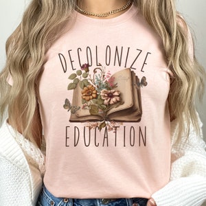 May include: A pink t-shirt with the text "DECOLONIZE EDUCATION" and a vintage book with flowers and butterflies.