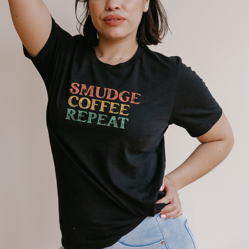 May include: A black t-shirt with the text "SMUDGE COFFEE REPEAT" in a retro font with colorful accents.