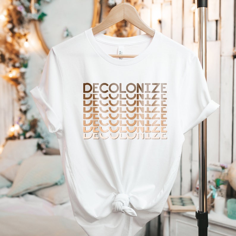 Puede incluir: Camiseta blanca con la palabra "DECOLONIZE" repetida en un degradado de tonos marrones.