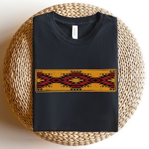 May include: Black t-shirt with a geometric pattern in red, yellow, and black. The pattern is reminiscent of Native American art.