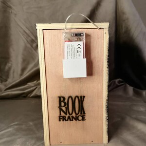 Puede incluir: Una caja de madera con una luz en su interior. La caja tiene una etiqueta negra que dice "BOOK NOOK FRANCE".
