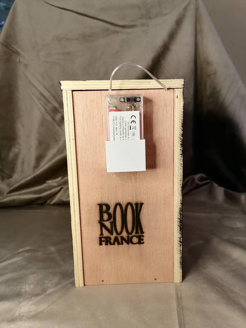 Puede incluir: Una caja de madera con una luz en su interior. La caja tiene una etiqueta negra que dice "BOOK NOOK FRANCE".