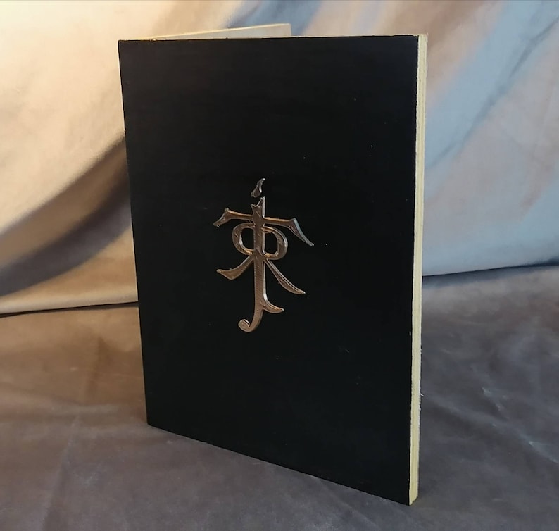 May include: A black book with a silver embossed symbol on the front cover. The symbol is a stylized letter "R" with a cross above it.