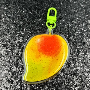 May include: A yellow and orange mango keychain with a green metal clasp. The mango is made of clear plastic with a glittery finish.