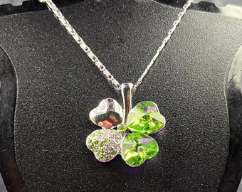 May include: A silver chain necklace with a four-leaf clover pendant. The clover is made of silver and has green crystal accents.